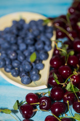 Summer, wild berries on the table. Closeup of blueberry and cherry on a blue background