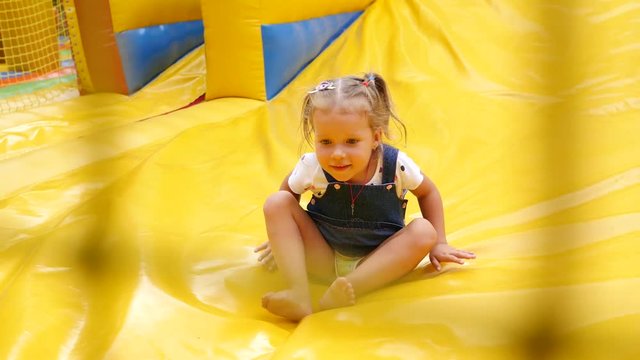Happy childhood - little kid girl slides down the inflatable slide outdoor trampoline