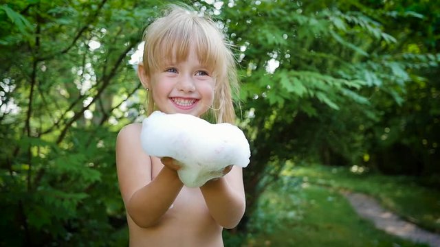 Little happy child girl have fun play blow a shampoo soap foam during washing outdoors