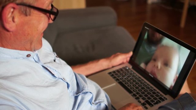 Grandfather sees his grandson for the first time through the Internet. Three generations of men, a happy family. A mature man talking to his son and grandson on skype