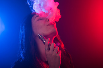 Portrait of young woman in neon red and blue smoke with vape or e-cigarettes