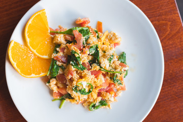 Frische Bio Rühreier mit Tomaten und Spinat auf einem weißen Teller in einem Frühstück-Cafe  serviert