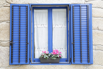 Window with blue shutters, on the windowsill, a potted with flowers