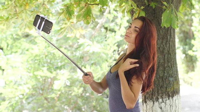 Taking selfie stick photo of cute busty girl posing with smart phone for social media