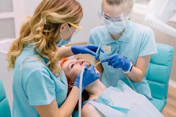 Wall murals Dentists young woman dentist treats teeth to her patient
