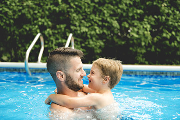 Cute little boy learning to swim with parents in pool