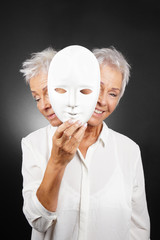 older woman hiding happy and sad face behind mask, concept for manic depression or bipolar or...
