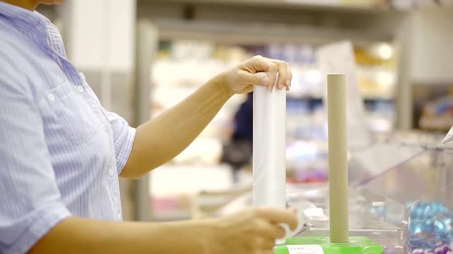 woman is spinning roll with plastic packages in a supermarket, tearing off, close-up of hands