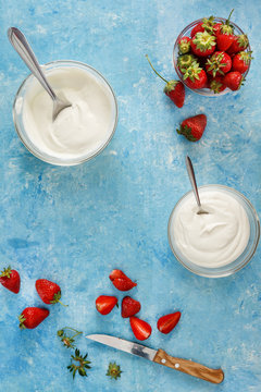 Organic yogurt in a bowl with freshly cut strawberries on a blue coOrganic yogurt in a bowl with freshly cut strawberries on a blue concrete background. Top view and close-up. Flatlay