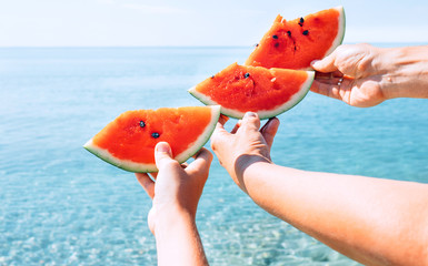 Three hands with watermelon segments are on azure calm sea water background