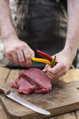 Men's hands and steaks of meat. Preparation of dinner man. Wooden table and old board. Beef and bitter colored pepper. Copy space.