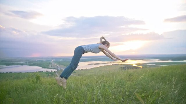 Young woman practicing acrobatic flip through the sun at sunset