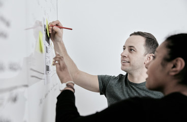 Man and woman discussing work and making notes on a whiteboard.  in an office. 