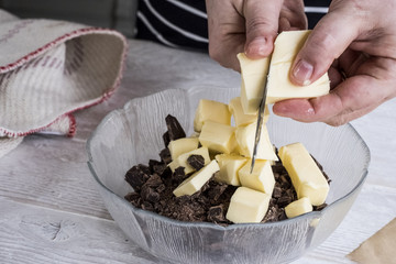 A person cutting chunks of butter into a bowl with pieces of chocolate. 