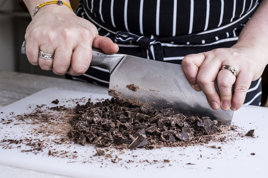 A cook chopping chocolate pieces with a large cleaver.
