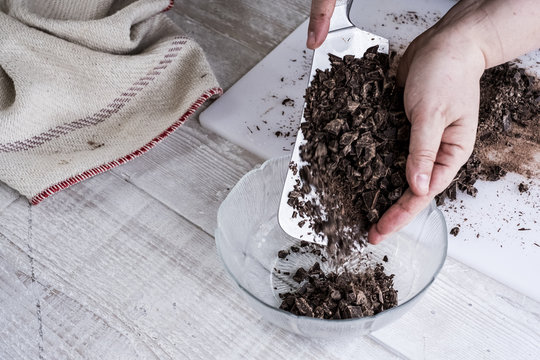 A cook holding a cleaver blade with chopped chocolate pieces. 