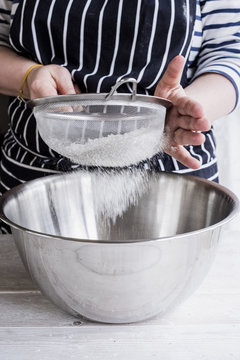A cook sieving ingredients through a sieve, flour into a metal bowl.