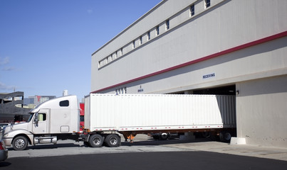 Semi truck with trailer backed into warehouse loading dock.