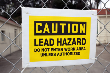 CAUTION LEAD HAZARD sign attached to chain link fence.