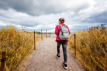 Girl traveler with a backpack walks around the island of Suomenlinna in a beautiful autumn day, a trip to nature in Northern Europe, Finland