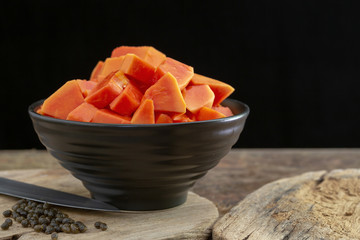 Ripe papaya fruit cut into pieces in a black bowl on wooden background