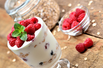 Greek yoghurt with oatmeal and fresh raspberries in a glass and mint leaves, full glass of oatmeals in background