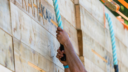 Two hands grab a rope to climb over a wall, obstacle course racing