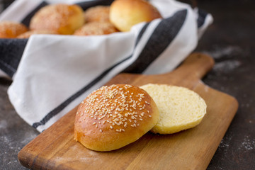 Homemade Hamburger Buns Topped with Sesame Seeds in Wire Bread Basket; One Cut open on Wood Cutting Board