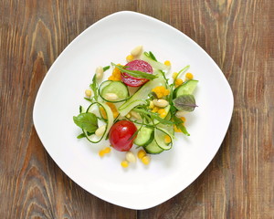 Fresh salad with zucchini, arugula, corn, cucumbers and tomatoes, top view