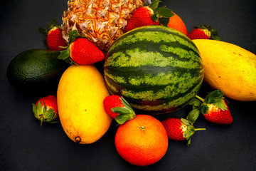 Watermelon, mango, strawberry, mandarin, pineapple and avocado on black background.
