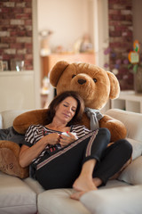 Beautiful best age woman lying on the couch relaxing, with a huge teddy bear, enjoying life, drinking coffee, carefree, happy mood 
