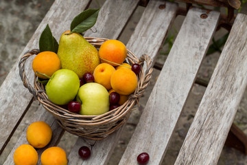 fruit basket is on the bench, it is composed of pear, apples, cherries and apricots