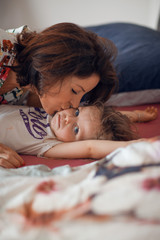 beautiful mother cuddles with her daughter in bed, giggling and laughing and kissing, beautiful...