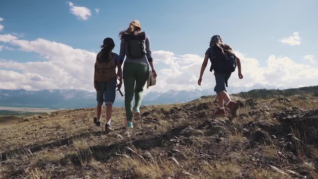 family of tourists. a young woman with children walking along a path in the mountains. A young mother and children with backpacks go on a hike. back view