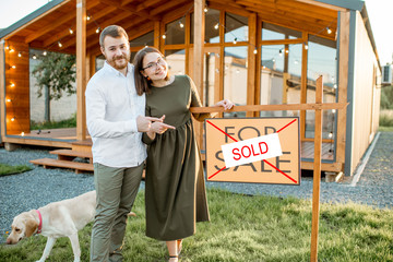Elegant and happy couple standing in front of their new and beautiful wooden country house