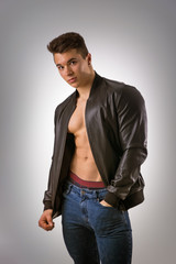 Handsome young muscleman with leather jacket on naked torso, isolated on white background in studio shot