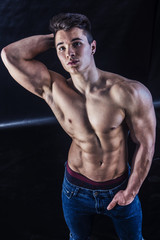Fototapeta na wymiar Handsome young muscular man shirtless wearing jeans, on dark background in studio shot