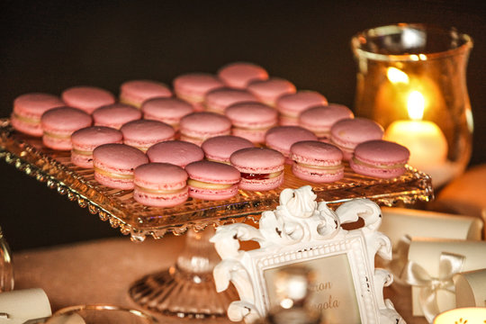 Macarons color rosa  sopra un vassoio argentato vicino a un tavolo con una candela