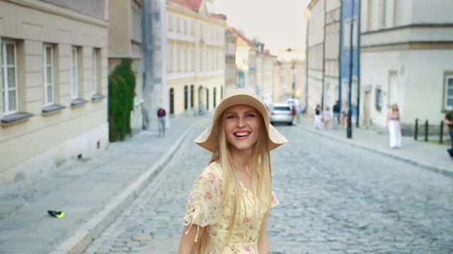 Smiling woman walking on street. Cheerful pretty woman in white hat looking back at camera while walking in town.