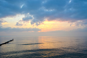 Fototapeta premium Blue and orange light while a sunrise over the Baltic Sea on Usedom, Germany, with wave-breakers and seagulls sitting on them against the light