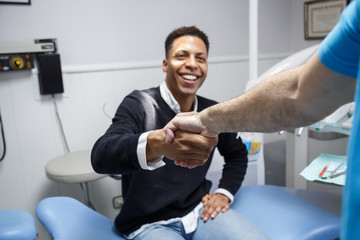Young African-American man shaking hand of crop dentist having visit in medical clinic. 