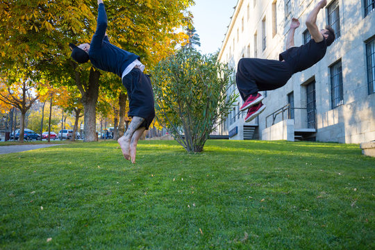 Two young men doing a side flip or somersault while they practicing parkour on the street. 