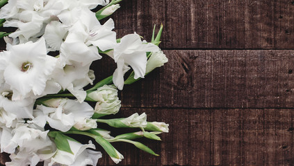 beautiful white gladioluses on rustic wooden background top view. stylish gladioli on rustic brown...