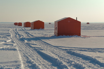 Ice fishing huts on a frozen lake in Ontario at sunset