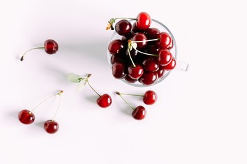 Obraz na płótnie Canvas Juicy cherry in a glass bowl. Ripe cherry berries and leaves isolated on white background. Berry summer background. Flat lay, top view, copy space 