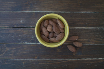 sweet almonds in a yellow bowl on a wooden table seen from above