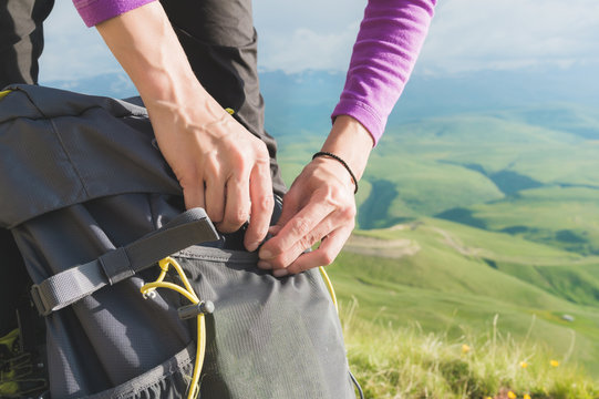 Close-up of women's hands unfasten the buckle on the camp backpack against the background of the valley in the setting sun. Tourism. Tracking