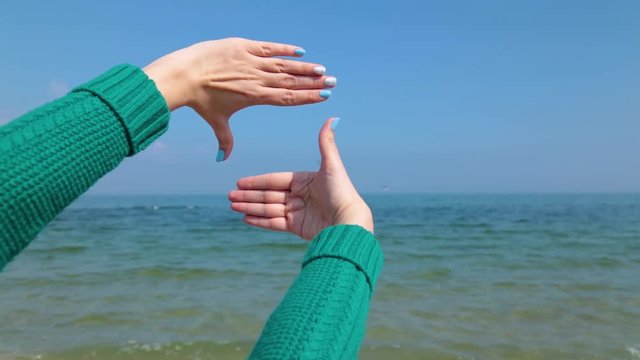 Closeup view of two female hands forming frame isolated at blue sea water and sky background. Point of view video footage.