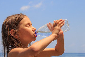 Closeup of young girl drinking fresh cold tap water from transparent plastic drinking bottle while outdoors on a hot summer day.