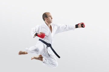An athlete in karategi trains a swings to hit with a hand in a jump
